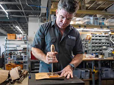 Gearheart Industry craftsman making a test burn with a branding iron at the workbench